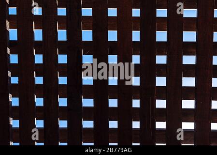 Wooden beam roof viewed from below with squares shapes, covering the sun, with a blue sky Stock Photo