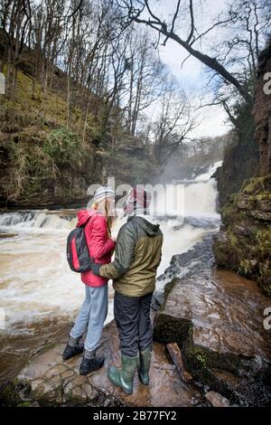 Walkers tread carefully on the banks of the River Mellte at the Sgwd Isaf Clun-Gwyn falls near Pontneddfechan in the Brecon Beacons, Wales, UK Stock Photo