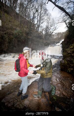 Walkers tread carefully on the banks of the River Mellte at the Sgwd Isaf Clun-Gwyn falls near Pontneddfechan in the Brecon Beacons, Wales, UK Stock Photo