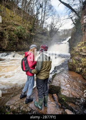 Walkers tread carefully on the banks of the River Mellte at the Sgwd Isaf Clun-Gwyn falls near Pontneddfechan in the Brecon Beacons, Wales, UK Stock Photo