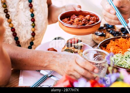 Close up with old senior hands taking food to eat from the table at home or restaurant - couple and friennds having lunch together with vegetariann an Stock Photo