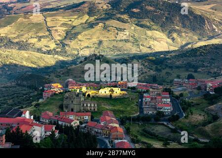 A group of houses with red roofs in a shady valley. Landscape of small sicilian village located under the hill. Stock Photo