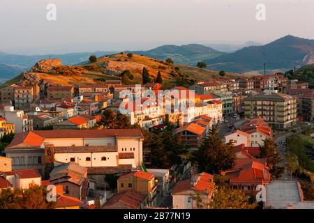 A group of houses with red roofs in a shady valley. Landscape of small sicilian village located under the hill. Stock Photo