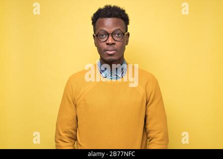 Young african american man in yellow sweater looking serious at camera. Stock Photo