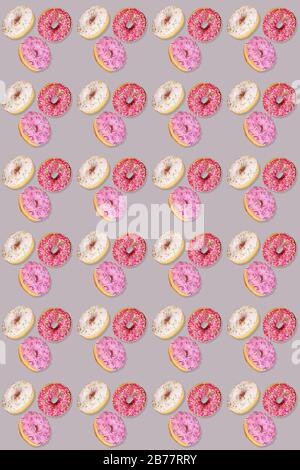 Trendy seamless pattern of traditional doughnuts with lilac, white and purple glazes on grey backdrop. Regular rhythmic pattern similar as grid. Top v Stock Photo