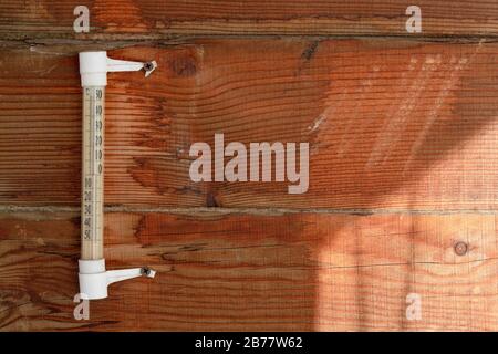A wooden wall of pine horizontal boards, a rough surface, an old mercury thermometer, warm sunlight. For the background of the weather. Stock Photo