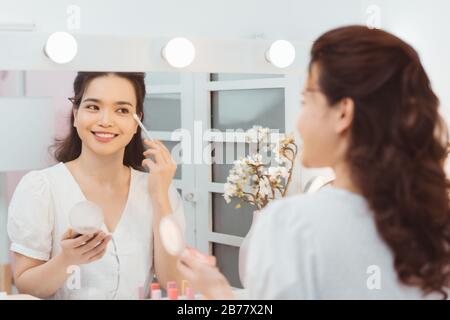 Young lady with pocket mirror using soft brush to smear eyeshadow Stock Photo