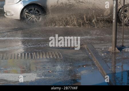 Vehicle car rides through spring puddles from melted snow. Spray from under the wheels. Stock Photo