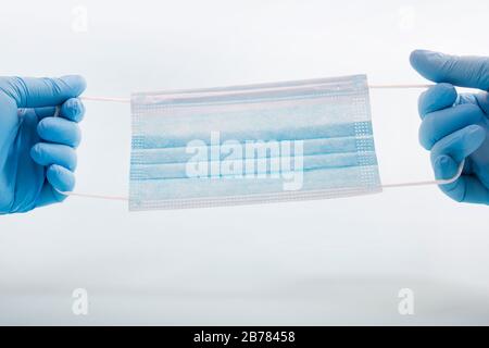 Doctor hand with blue gloves holds Medical protective masks isolated on a light blue background. Stock Photo