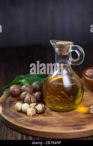 Natural macadamia oil in a glass bottle with macadamia nuts on wooden board Stock Photo