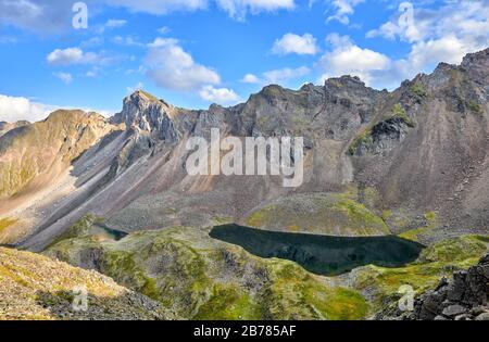 Deep dark lake in a hanging valley under a mountain range. Several lakes are located steps down. Eastern Sayan. Russia Stock Photo