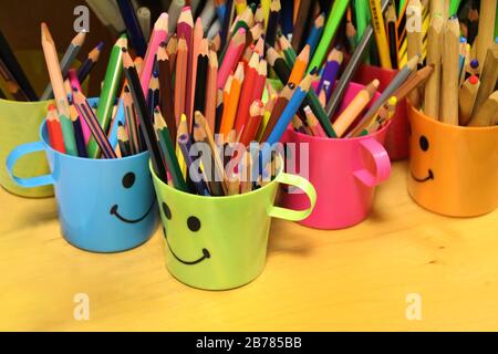 Close view of colored pencils on smiley cups on a school. Stock Photo