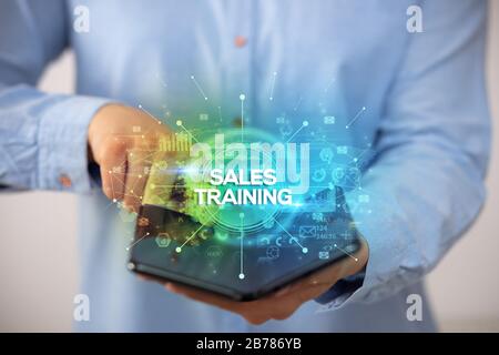 Businessman holding a foldable smartphone with SALES TRAINING inscription, new business concept