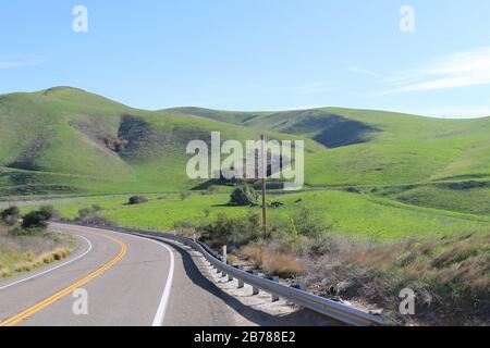 a winding curved road with bright mountain hillside and blue sky Stock Photo