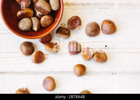 Brown chestnuts in bowl over white wooden surface. Stock Photo