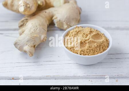 Grounded ginger and ginger root on white wooden surface. Stock Photo