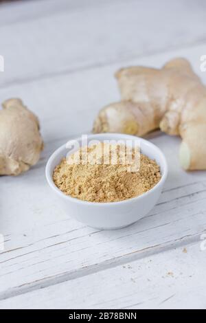 Grounded ginger and ginger root on white wooden surface. Stock Photo