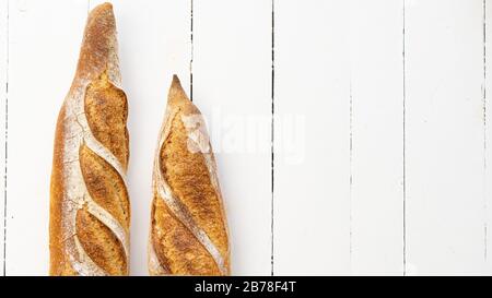 Two french baguettes on a left side on a white wooden table.  Stock Photo
