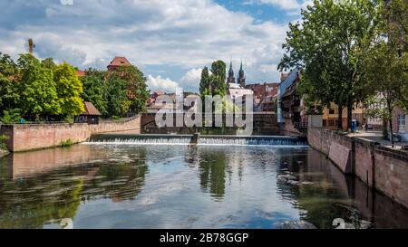 Nuremberg 2019. Max bridge over the Pegnitz river seen between the trees and the banks. We are on a sunny but cloudy summer day. August 2019 in Nuremb Stock Photo