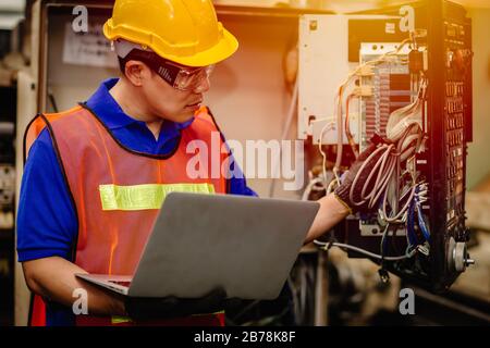 Service engineer team working with electronic wire back panel of heavy industry machine for maintenance repair and fix with laptop computer for analys Stock Photo