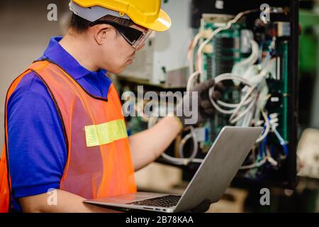 Service engineer team working with electronic wire back panel of heavy industry machine for maintenance repair and fix with laptop computer for analys Stock Photo