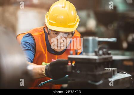 Asian Chinese engineer worker wearing safety suit helmet and eyes protection glasses focus at work inspection and checking production process on facto Stock Photo