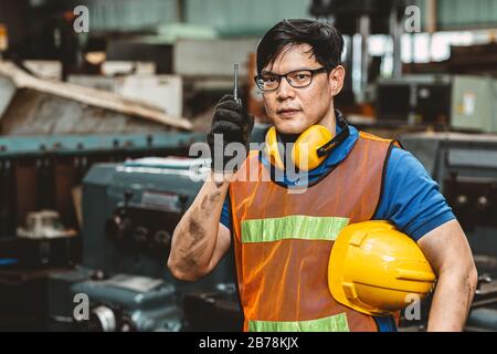 Asian engineer worker with protection suit set hard working in factory handle communication radio looking camera and smile. Stock Photo