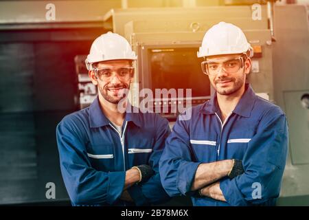 two worker engineer man standing  arm folding smiling with machine in heavy industry factory. Stock Photo