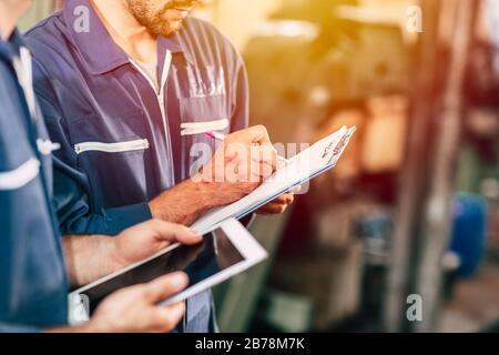worker taking note using pen and paper with new young engineer using computer tablet for work faster and more efficiency. Stock Photo