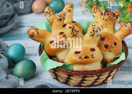 Easter Buns in the form of hares with multi-colored eggs are located in a wicker basket on a blue background, culinary idea for children Stock Photo