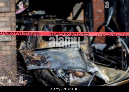 Twisted burnt metal of car after fire close up. Vehicle destroyed by flames. Burnt car and house after large fire. Stock Photo