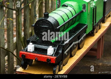 A miniature green model steam train in the rain at Stogumber station on the West Somerset Railway heritage line, Somerset, England Stock Photo