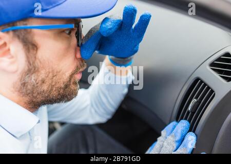 Car wash employee covering his nose with hand because of stink from air duct vent grille. Stock Photo