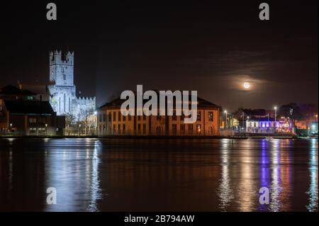 The rising moon in Limerick City with court house and St Mary's Catherdral and the boat house in lights. Stock Photo