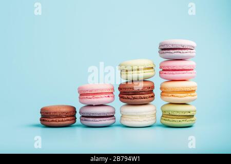 Macaroni cookies of different colors are arranged in the shape of pyramid steps on a blue background. Stock Photo
