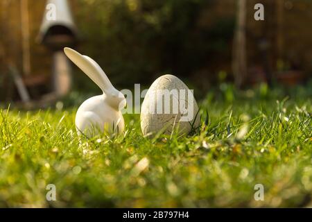 White bunny figurine near an egg in a green grassy field with a blurred background Stock Photo