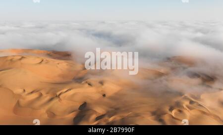 Aerial view of a massive sand dune surrounded by winter morning fog cloud in Empty Quarter. Liwa desert, Abu Dhabi, United Arab Emirates. Stock Photo