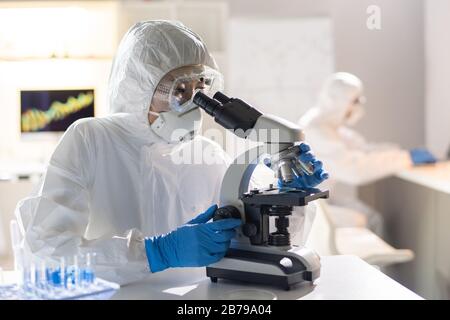 Female lab worker or researcher looking at new chemical element or virus molecule in microscope during scientific study Stock Photo