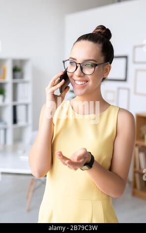 Pretty young smiling agent with smartphone explaining terms of agreement to one of clients during work in office Stock Photo
