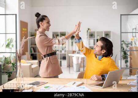 Two happy young successful colleagues giving each other high five after finishing work over new project in office environment Stock Photo