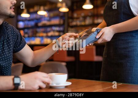 Client of contemporary cafe or restaurant making order and holding plastic card over payment machine while paying to waitress Stock Photo