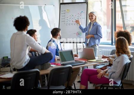 Smiling woman demonstrating presentation on board while talking with partners during job Stock Photo