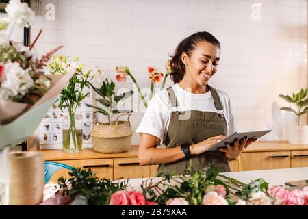 Young female florist making notes on a digital tablet. Woman checking online orders in shop. Stock Photo
