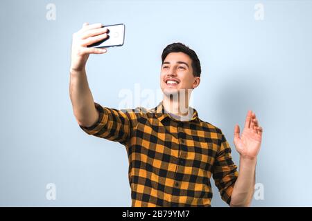 good looking young man in casual yellow shirt video-chatting via smartphone isolated against light blue background Stock Photo