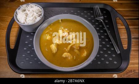 A bowl of thick Chinese king prawn takeaway / takeout curry on a plastic tray, next to a bowl of boiled / steamed rice and a fork, ready to eat. Stock Photo