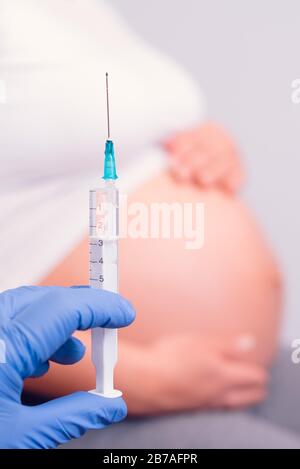Pregnant woman having medicine injection. Hand with blue gloves holding syringe in front of the pregnant belly. Stock Photo