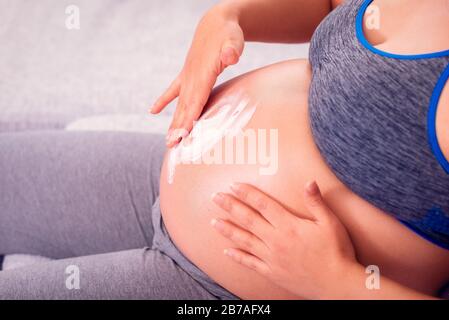 Pregnant woman rubbing her belly with body lotion against stretch marks on the skin during pregnancy.