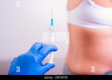 Pregnant woman having medicine injection. Hand with blue gloves holding syringe in front of the pregnant belly. Stock Photo