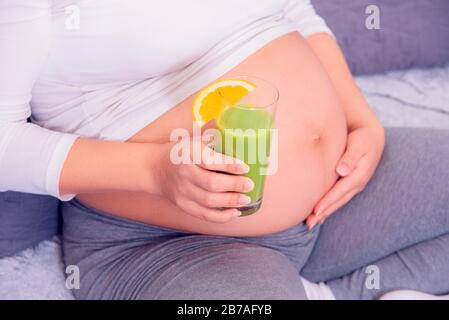 Pregnant woman enjoying her healthy organic green juice while relaxing on the couch at home. Stock Photo