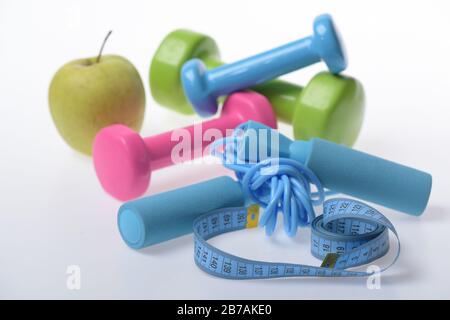 Skipping rope and barbells in green, blue and pink next to measure tape. Fit shape and sport concept. Health regime and fitness symbols. Dumbbells near apple and blue jump rope on white background Stock Photo